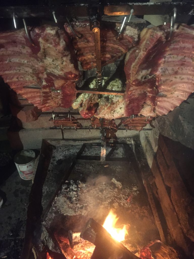 Fully loaded asado cross with several cuts of meat slow roasting over a fire.